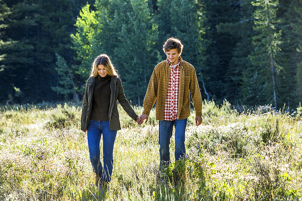 Caucasian couple walking in field holding hands