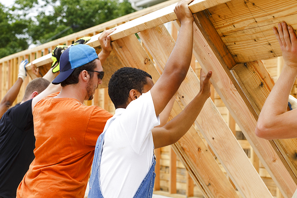 Volunteers lifting framed wall at construction site