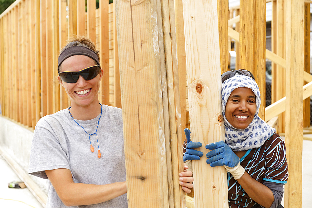 Smiling volunteers holding lumber at construction site