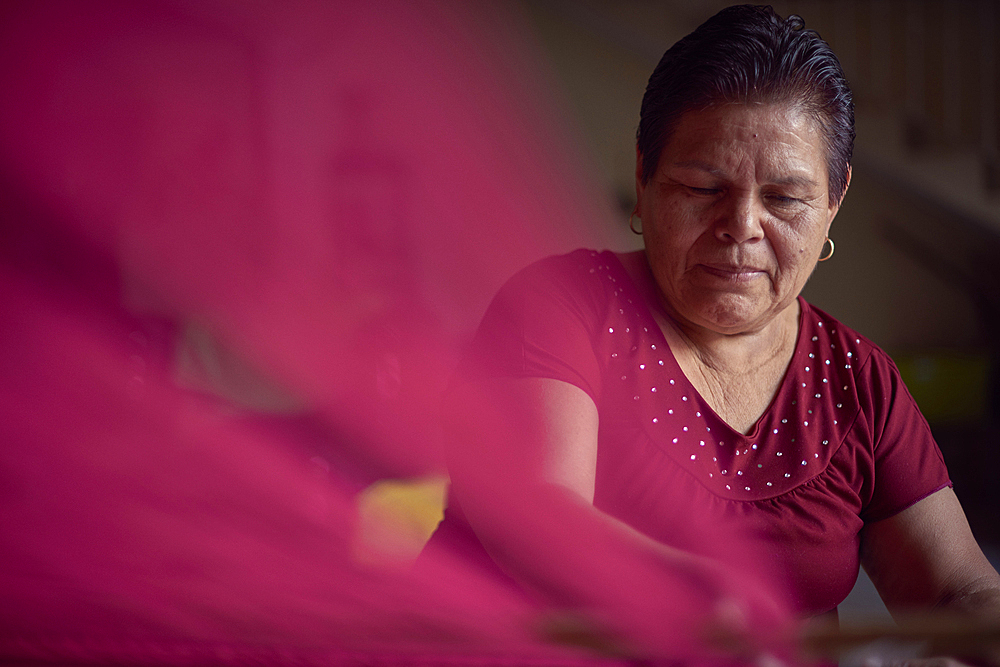 Hispanic woman weaving fabric on loom