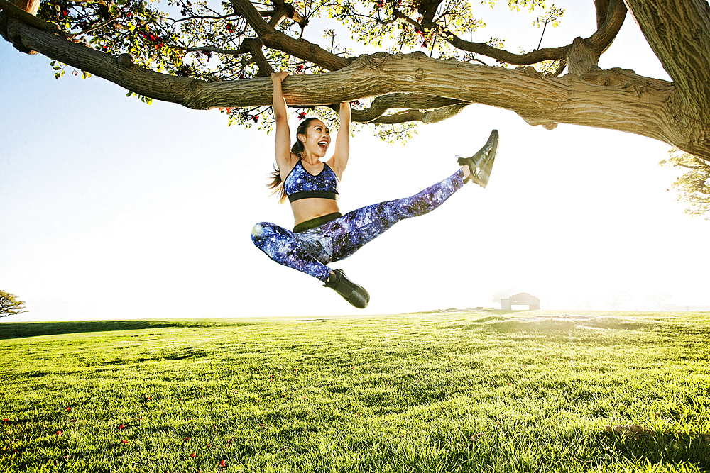 Happy mixed race woman hanging on tree branch