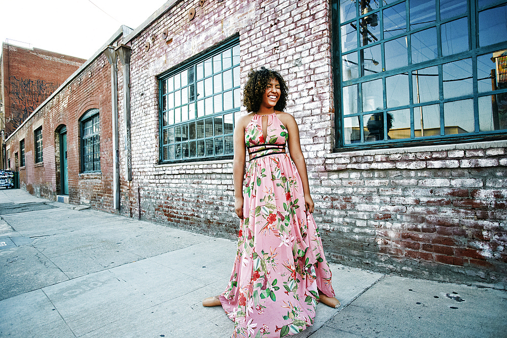 Smiling mixed race ballet dancer wearing dress on sidewalk