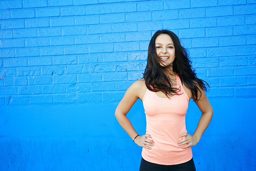 Wind blowing hair of smiling mixed race woman at blue wall