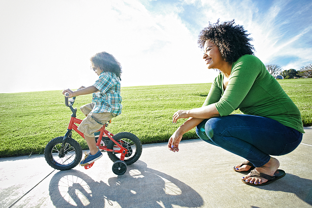 Mixed race mother watching son ride bicycle