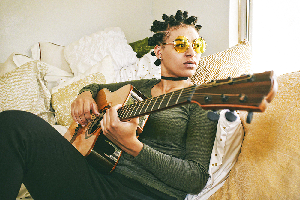 Mixed Race woman sitting on bed playing guitar