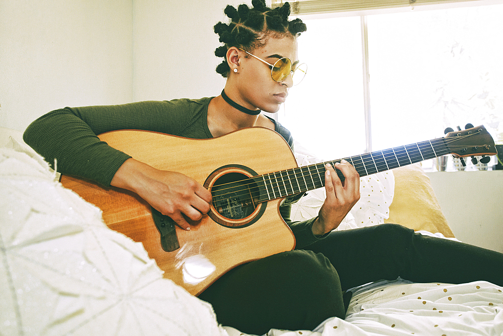 Mixed Race woman sitting on bed playing guitar