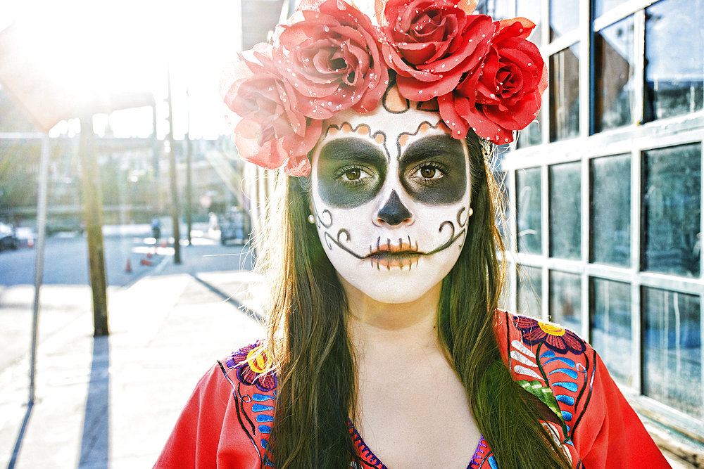 Hispanic woman on sidewalk wearing skull face paint