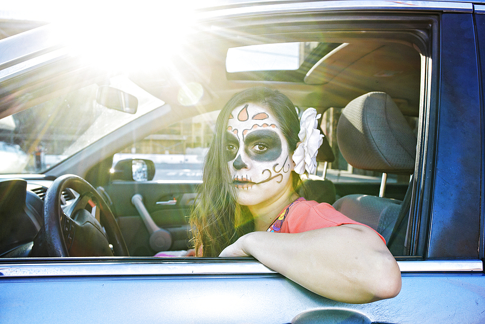 Hispanic woman driving car wearing skull face paint