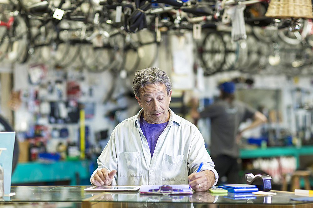 Caucasian man in bicycle shop writing on clipboard