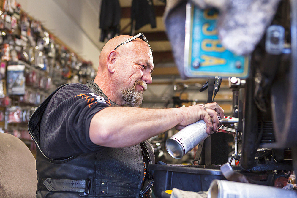 Caucasian man spraying lubricant on motorcycle