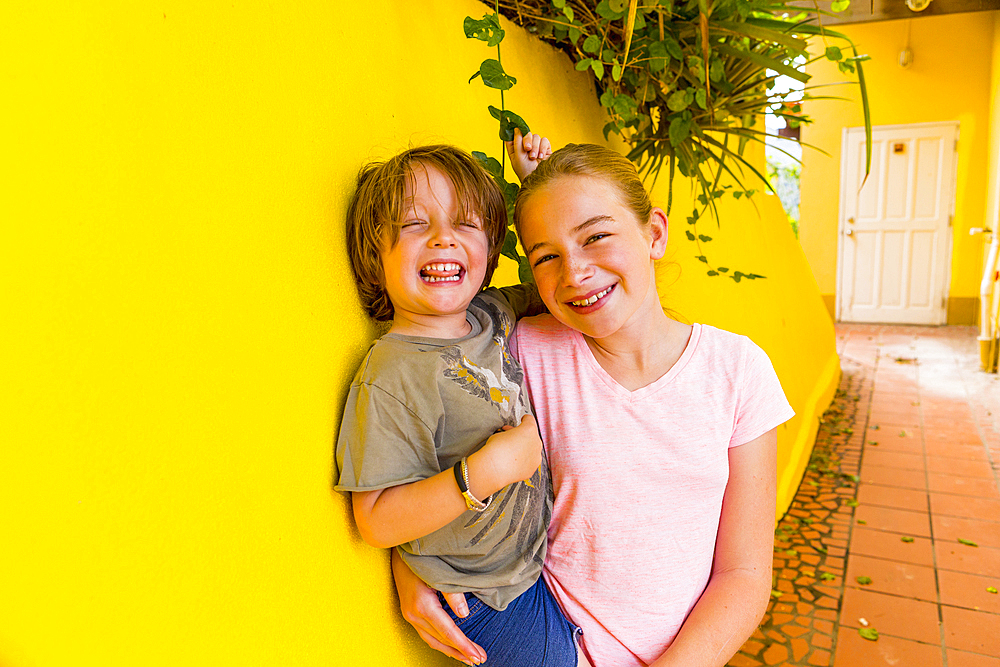 Caucasian girl leaning on yellow wall holding brother