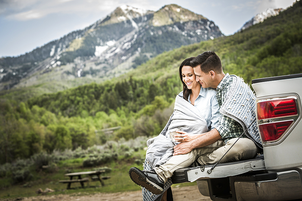 Couple wrapped in blanket sitting on bed of pick-up truck