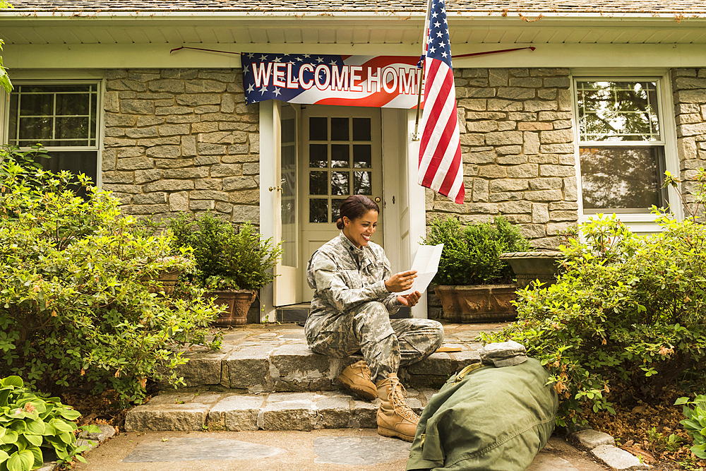 Smiling African American soldier sitting on front stoop reading letter