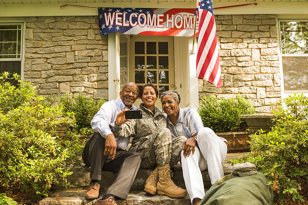 Soldier and parents sitting on front stoop posing for cell phone selfie