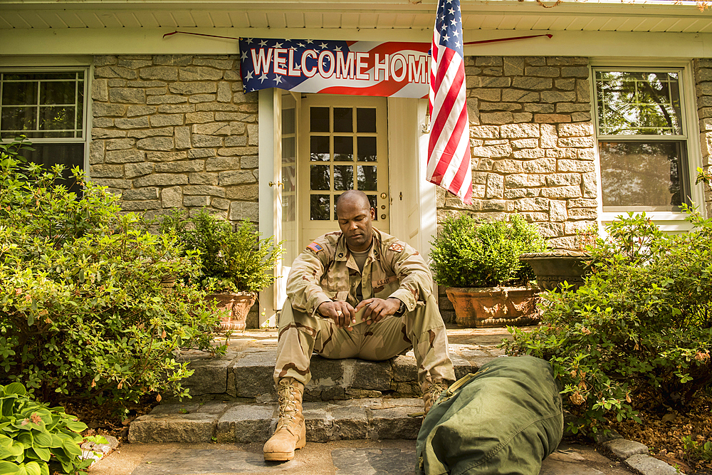 Frustrated African American soldier sitting on front stoop