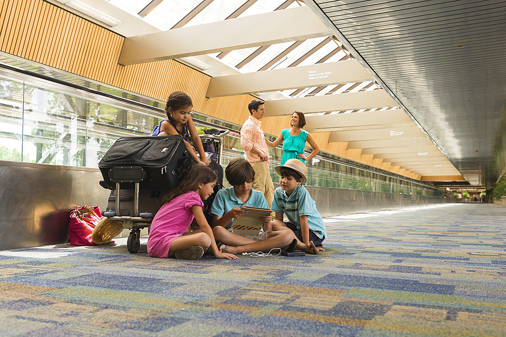 Children waiting in airport with family and using digital tablet