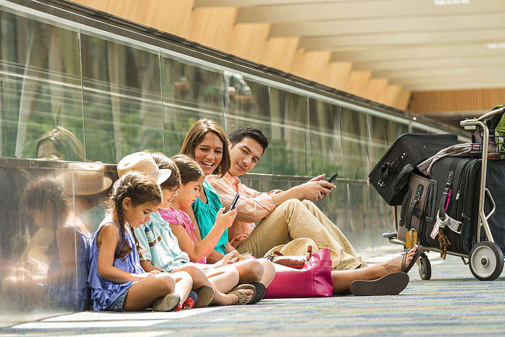 Family waiting on floor of airport using cell phones