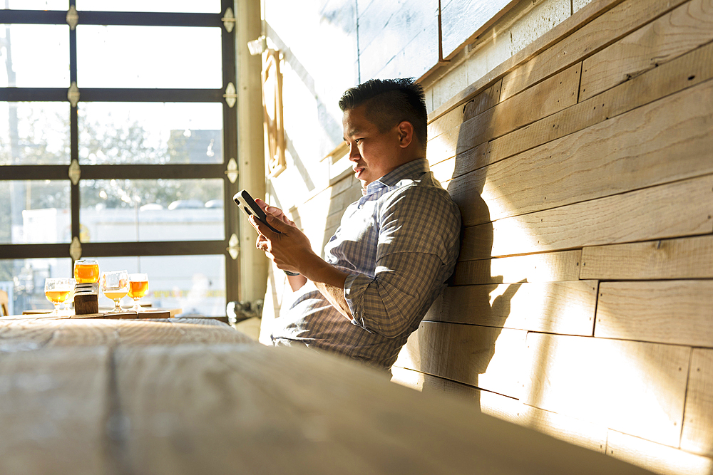 Asian man texting on cell phone in brew pub