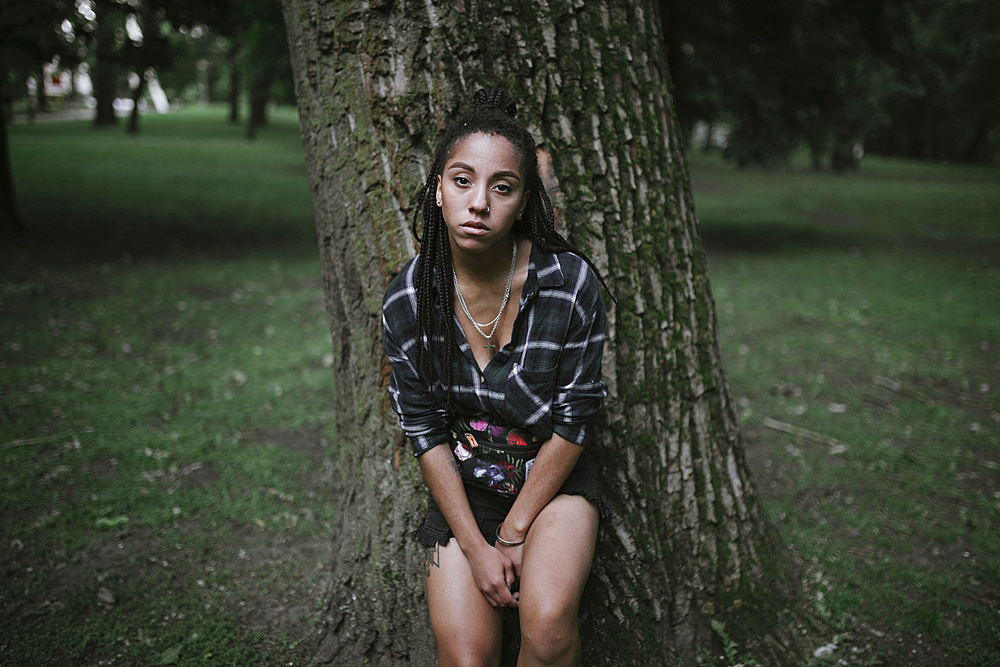 Portrait of serious African American woman leaning on tree