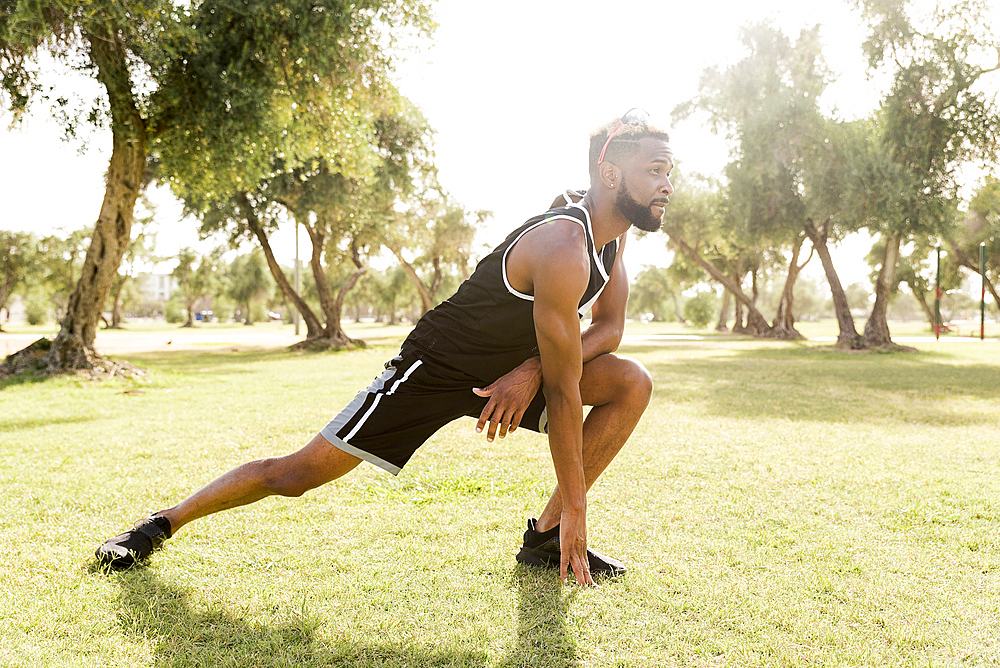 Black man crouching in park stretching legs