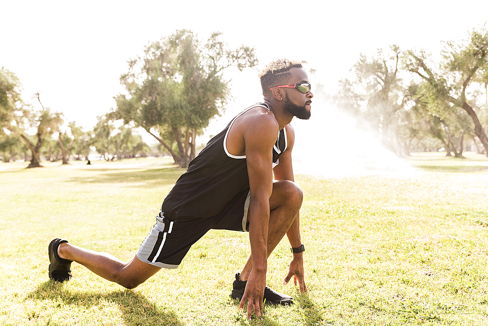 Black man crouching in park stretching legs