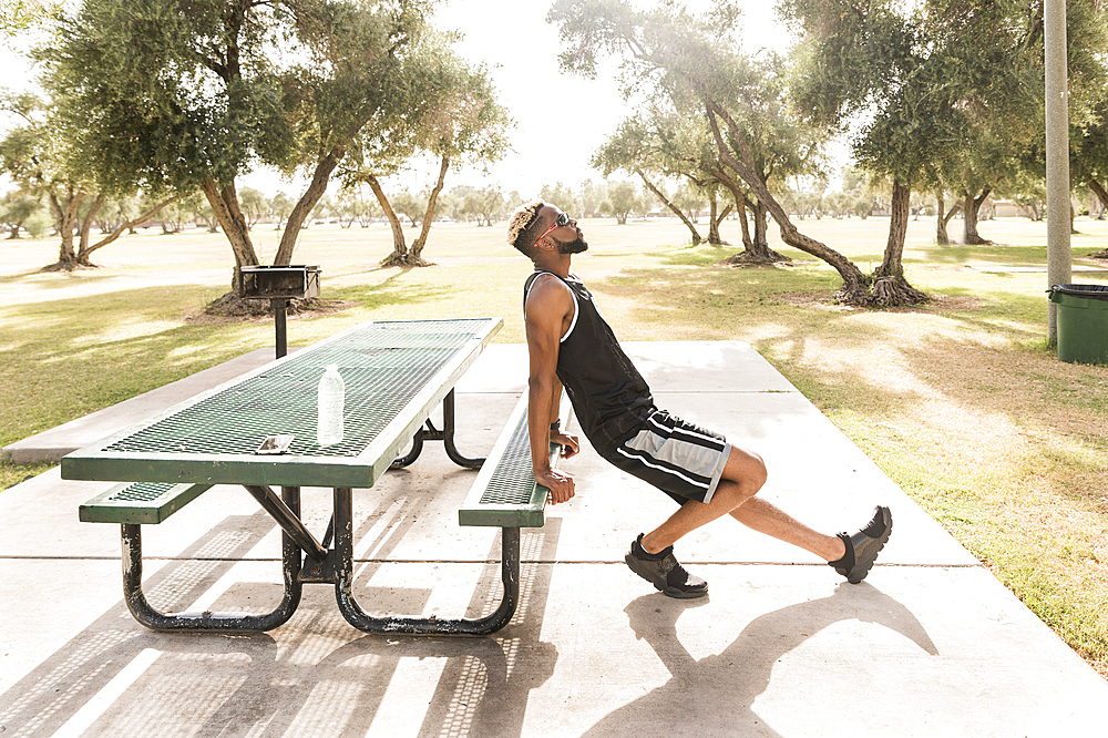 Black man leaning on picnic table in park stretching leg