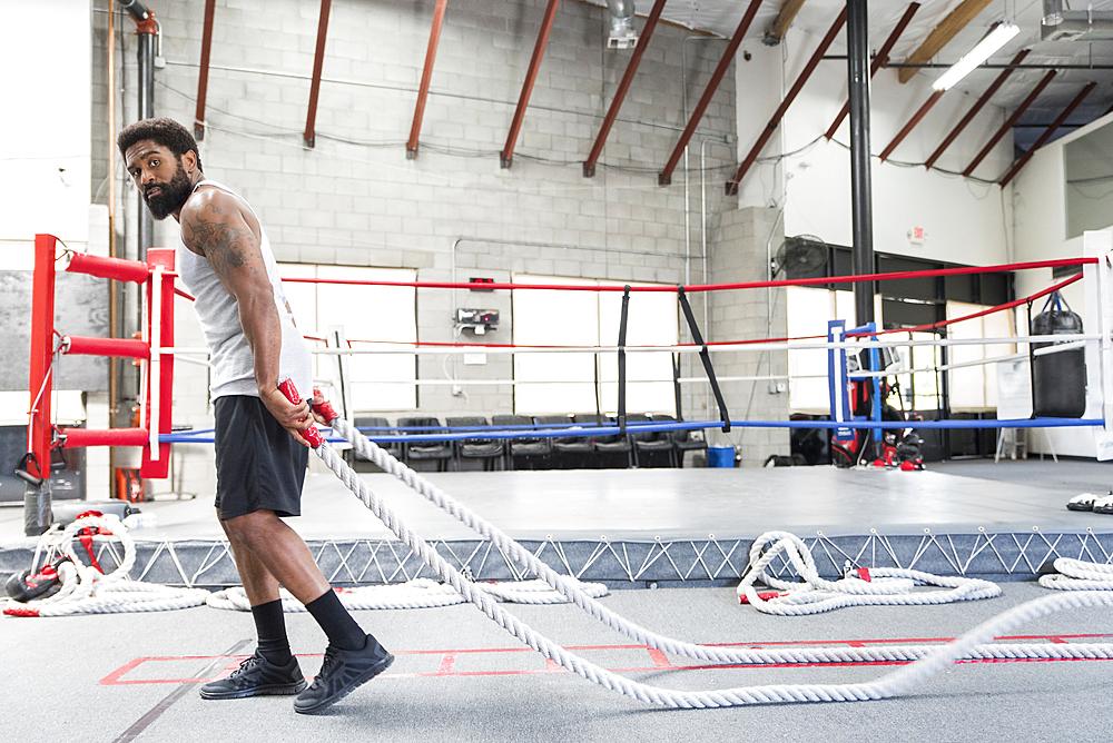 Black man pulling heavy ropes in gymnasium