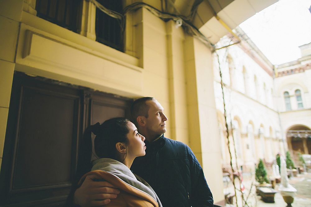 Caucasian couple hugging and leaning on wall in courtyard