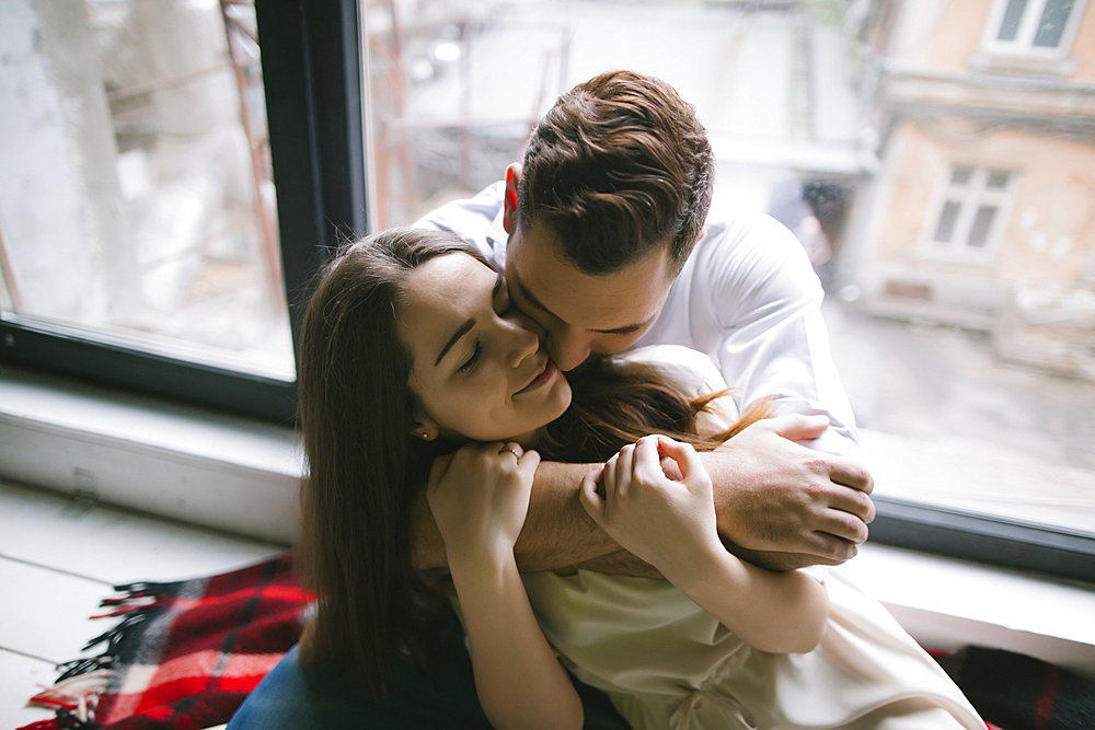 Caucasian couple hugging on bench near window