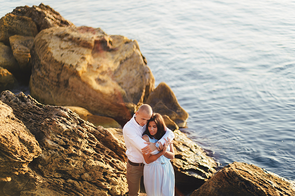 Caucasian couple hugging on rocks on beach