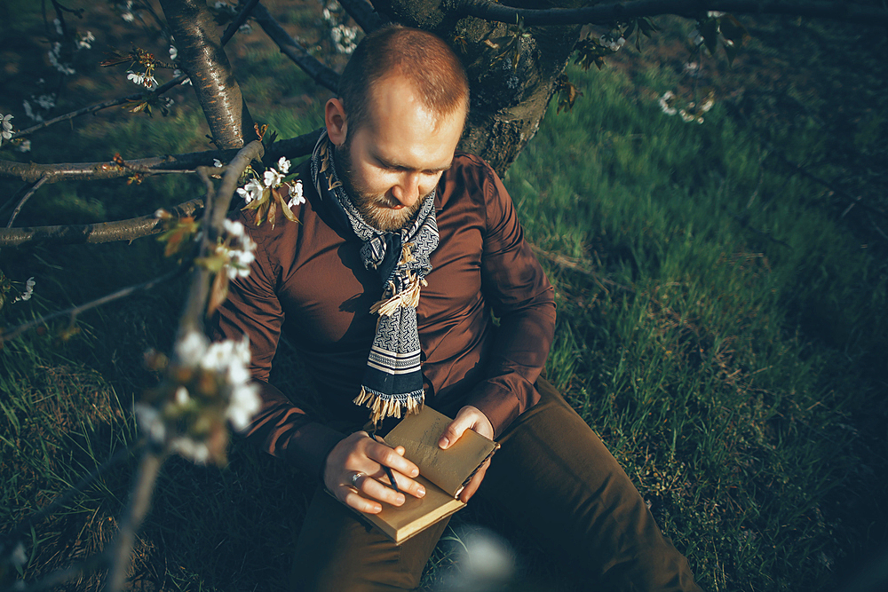 Caucasian man leaning on tree writing in journal