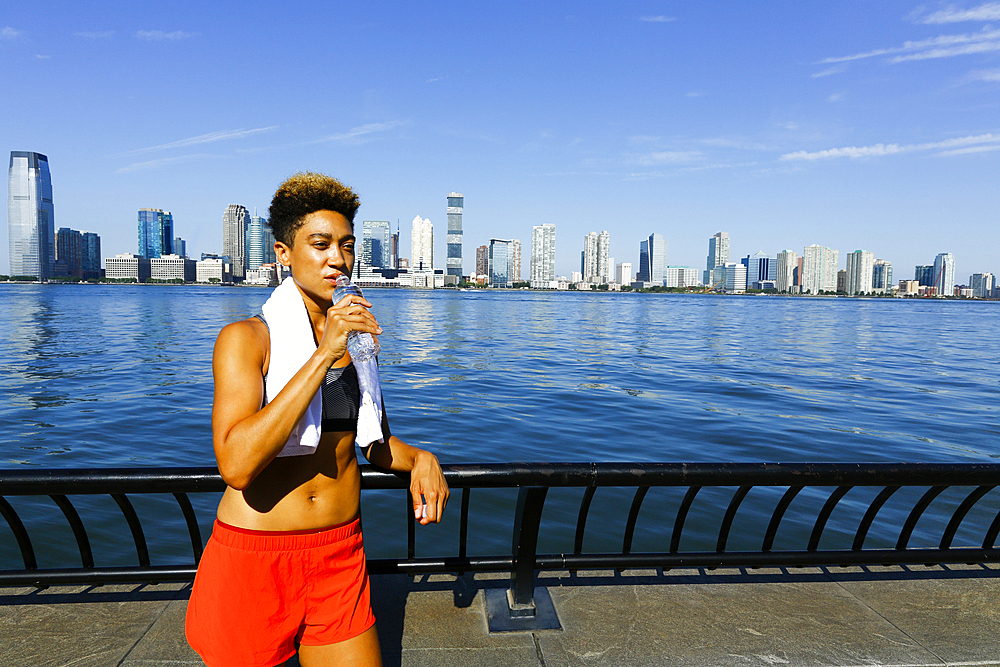 Mixed race woman drinking water from bottle at waterfront