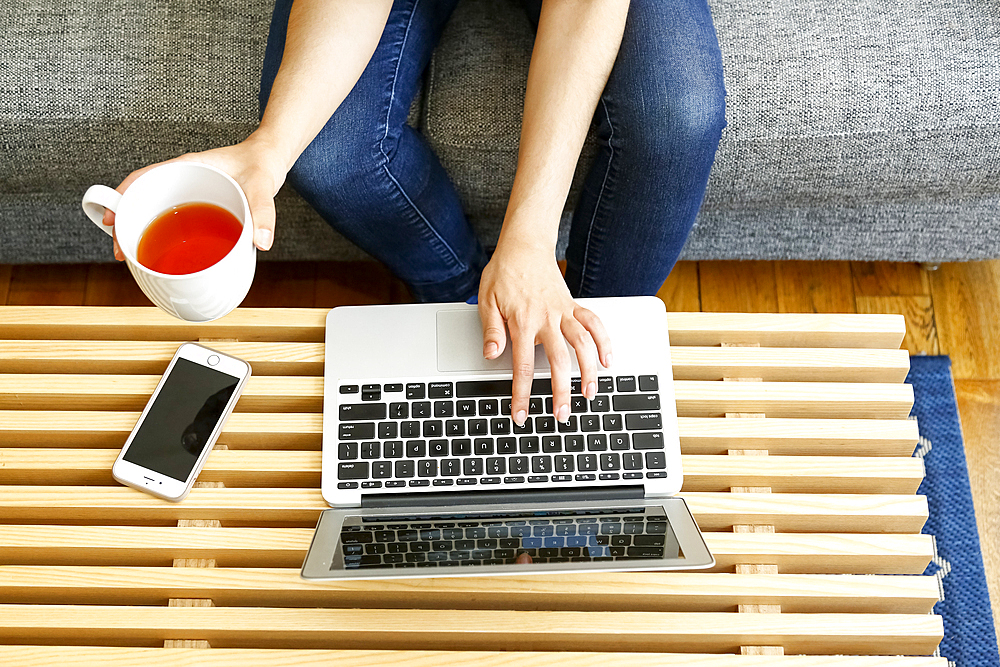 Hands of mixed race woman using laptop and drinking tea