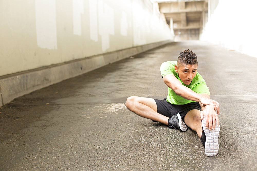 Mixed Race man sitting on ground stretching leg