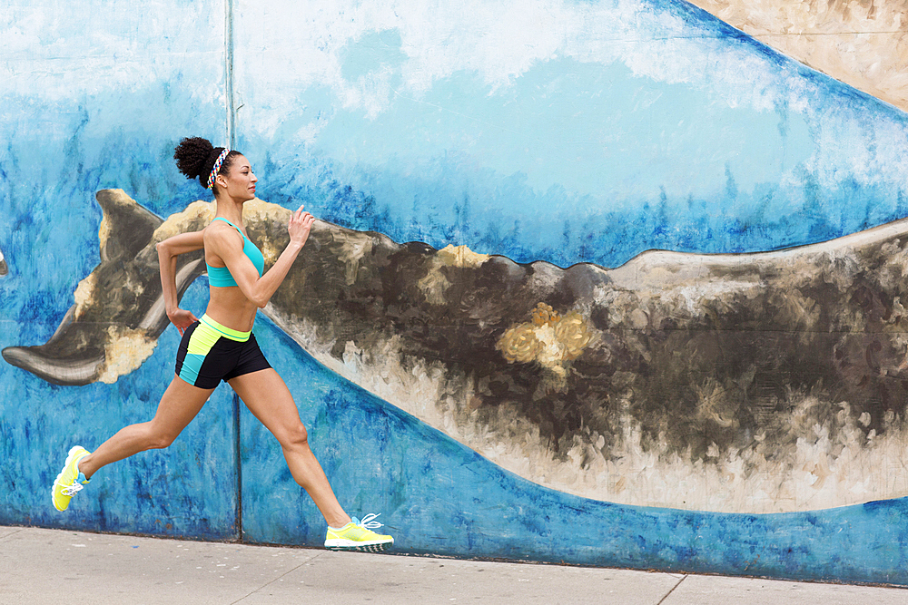 Mixed Race woman running on sidewalk near mural