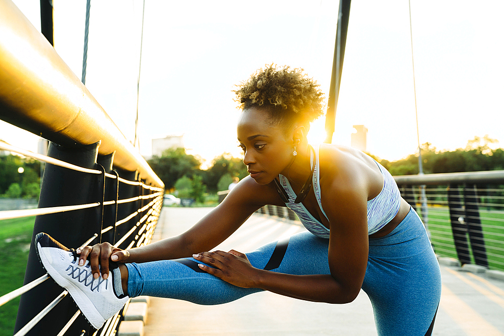 Mixed race woman stretching leg on bridge railing