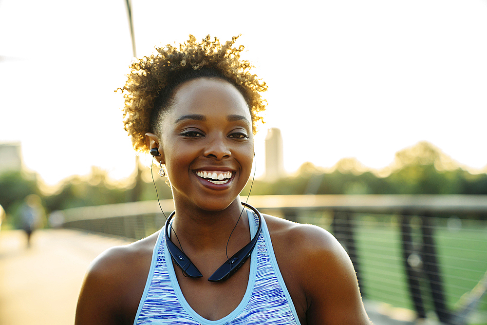 Smiling mixed race woman listening to earbuds on bridge