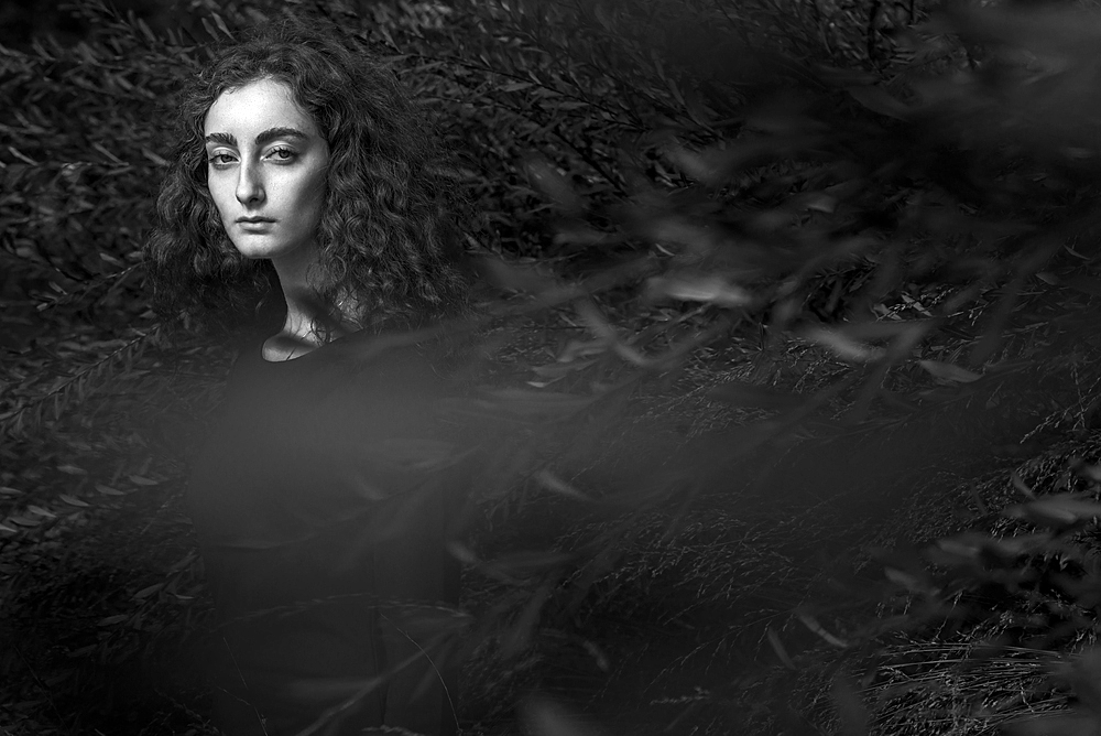 Serious Caucasian woman standing behind branches