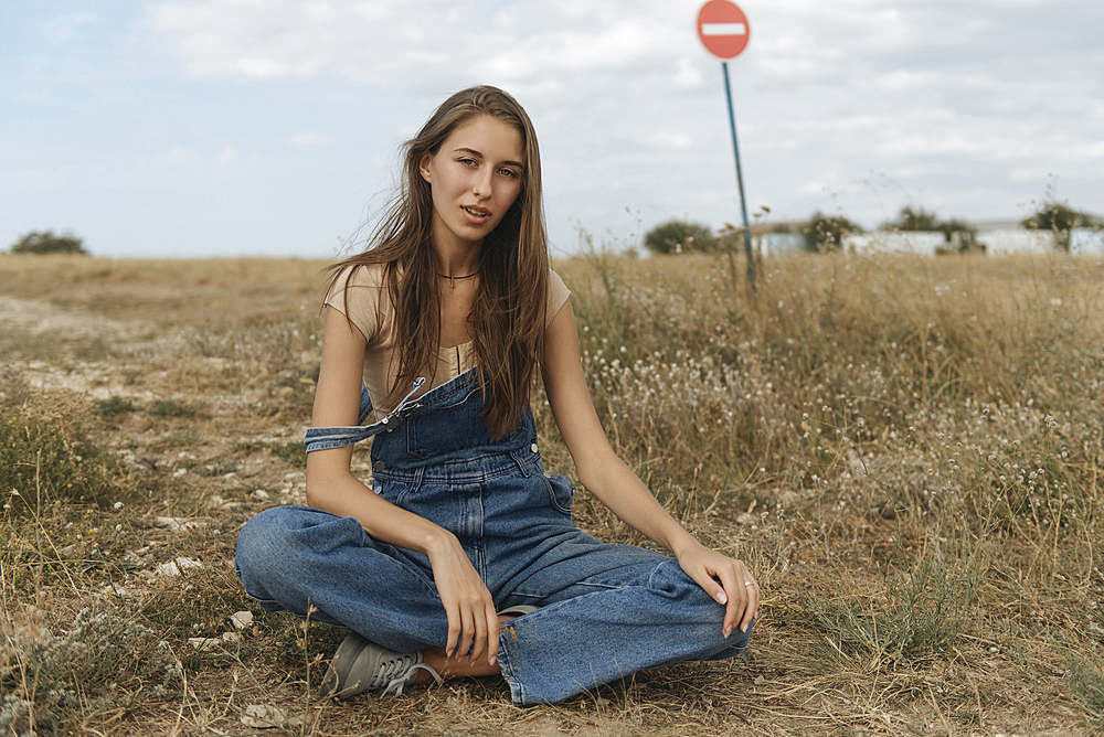 Caucasian woman wearing overalls sitting in rocky field