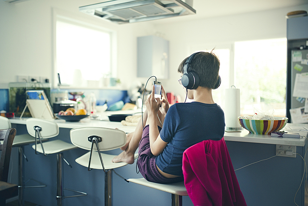 Mixed race boy sitting in kitchen listening to cell phone