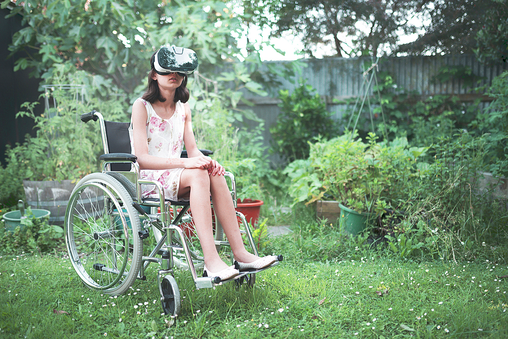 Mixed race girl in wheelchair using virtual reality goggles in backyard