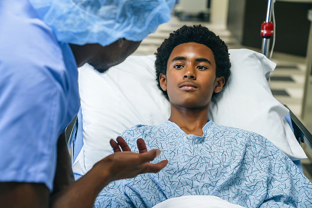 Black doctor talking to boy in hospital bed