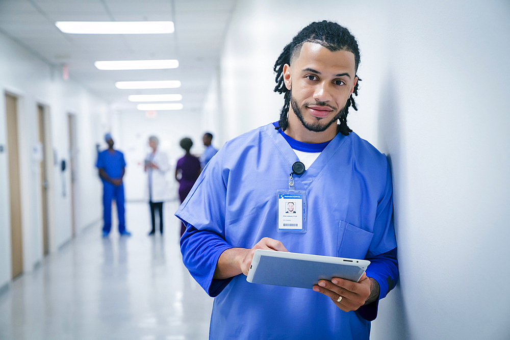 Smiling nurse leaning on wall in hospital using digital tablet