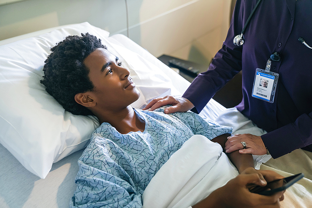 Doctor comforting boy in hospital bed holding cell phone