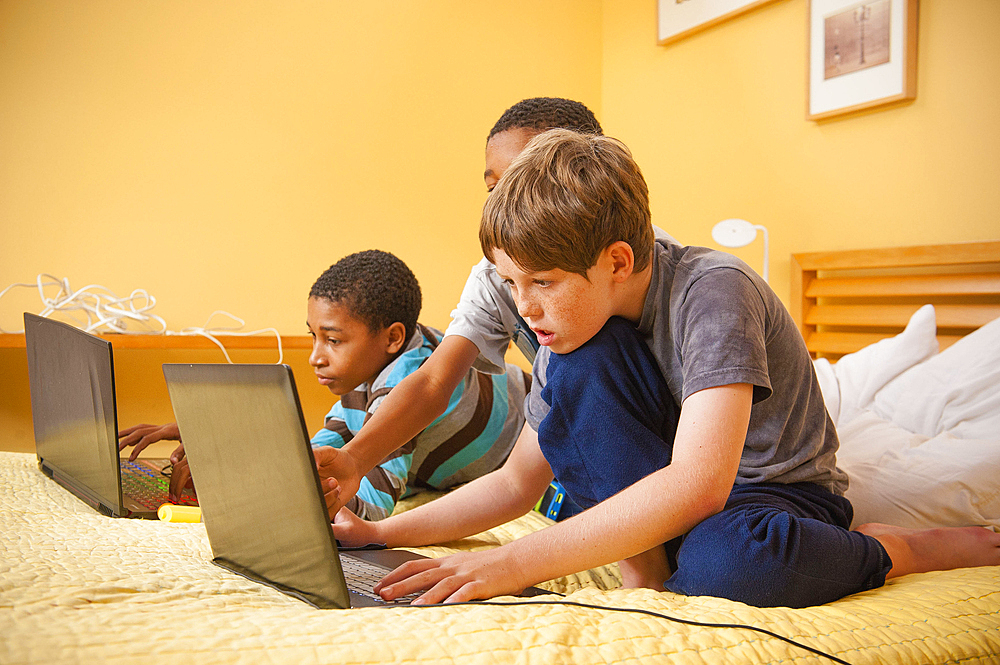 Boys sitting on bed using laptops