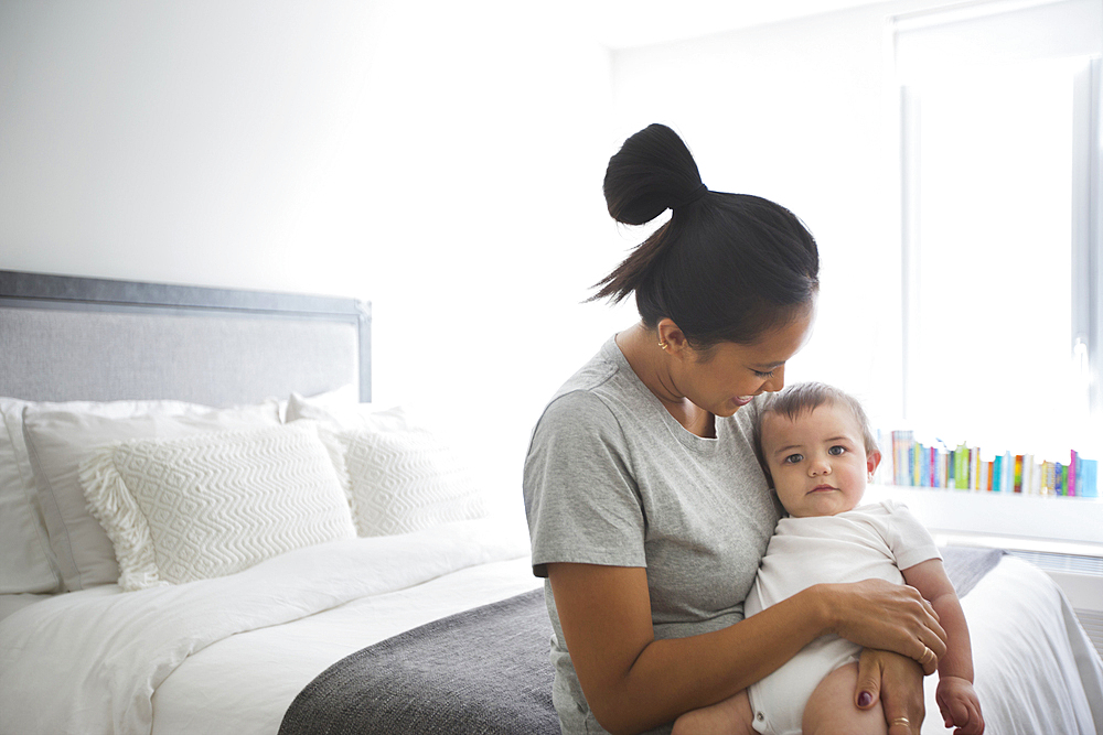 Mother holding baby son in lap on bed