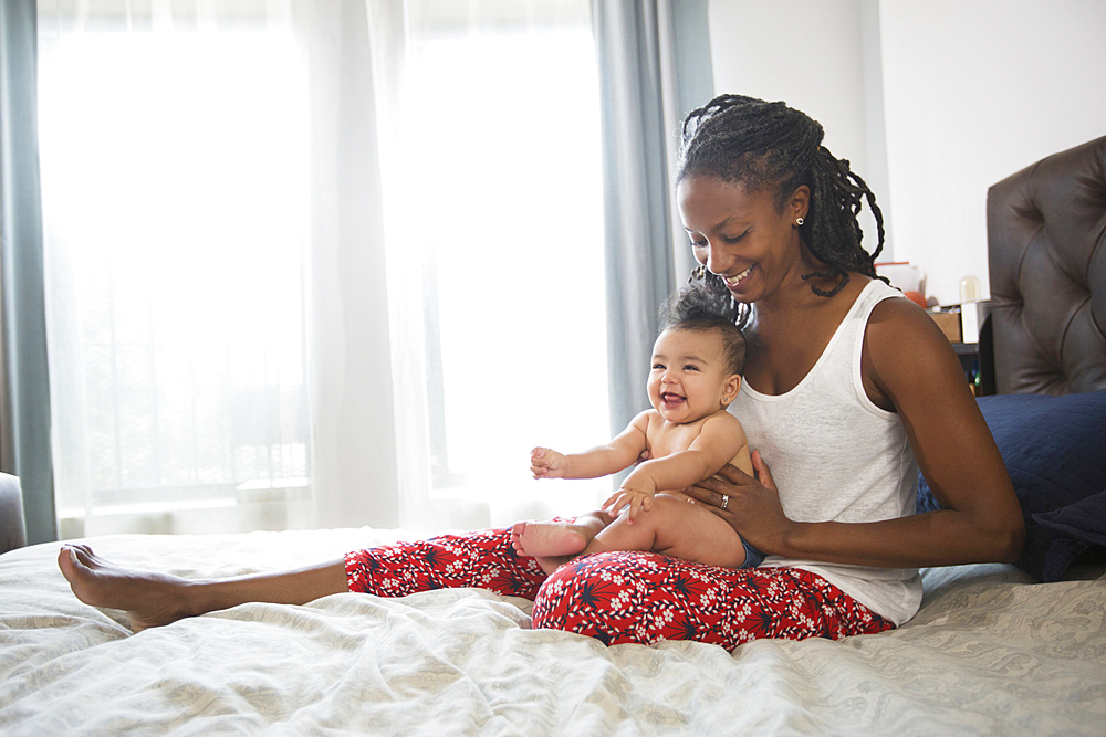 Mother sitting on bed holding baby daughter on lap