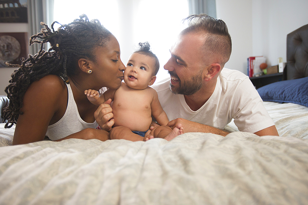 Mother and father laying on bed with baby daughter