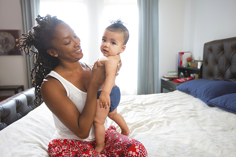 Mother sitting on bed holding baby daughter