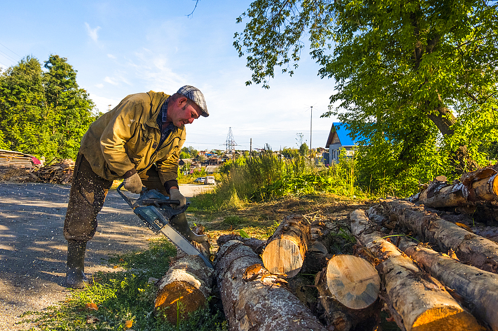 Caucasian man cutting logs with chainsaw